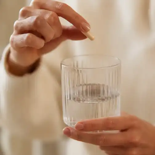 Une gélule tenue à la main devant un verre d'eau